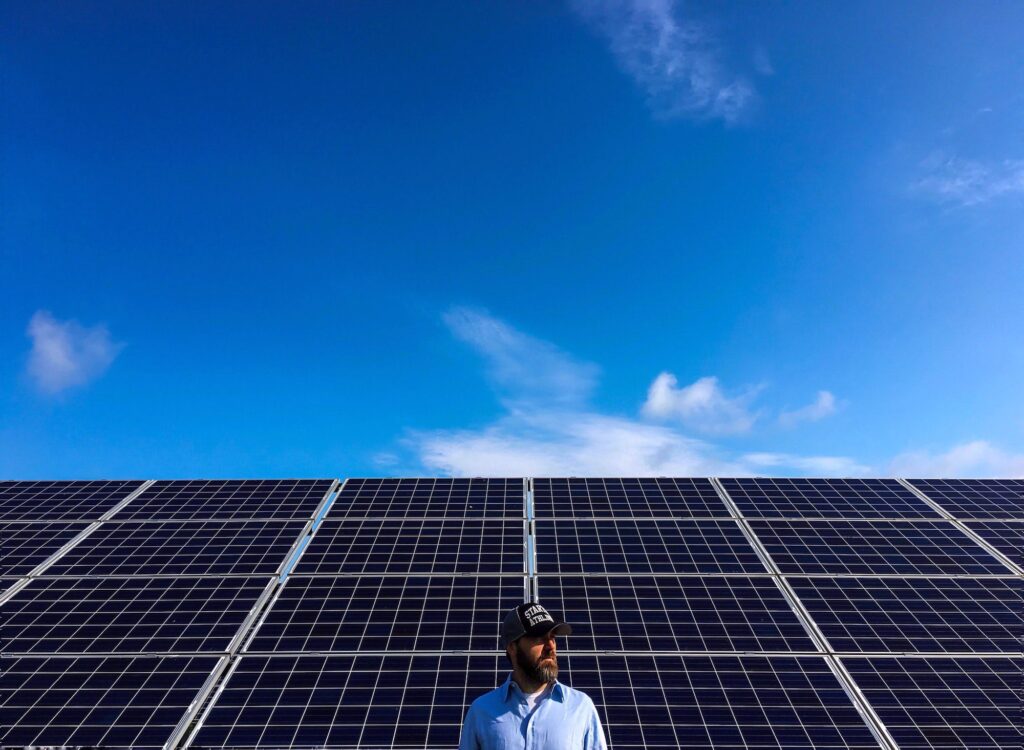 Man staat onder een rij zonnepanelen tegen een blauwe lucht
